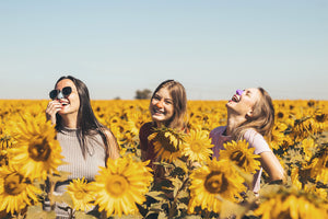 Three young, happy girls wearing colorful noz spf sunscreen on face surrounded by sunflowers